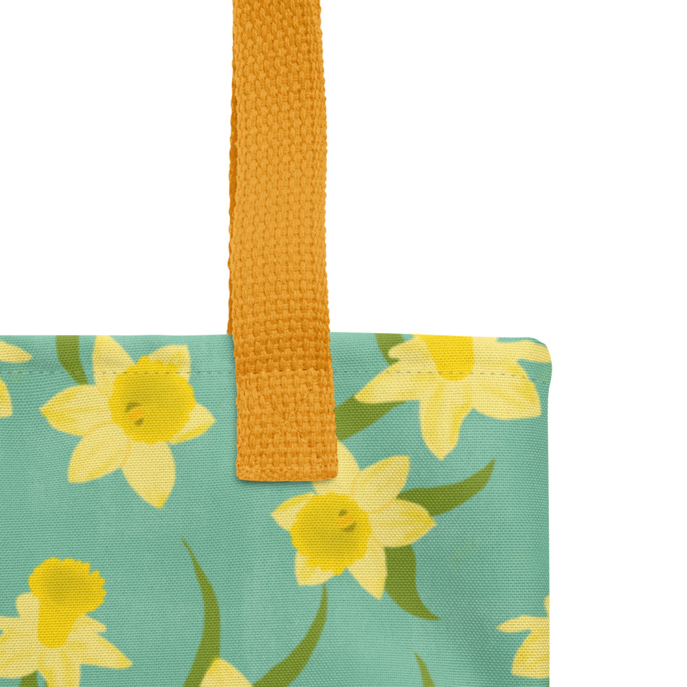 Close up of tote bag with yellow Daffodil floral pattern on a teal background by Carmel Rimmer. Item is photographed on a white background.
