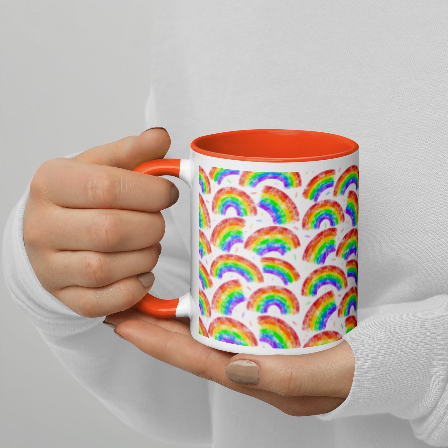 Mug with rainbow pattern by Carmel Rimmer and a orange interior held by a person against a plain background