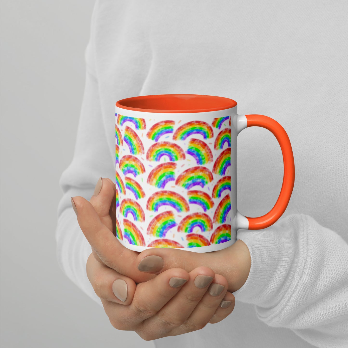 Mug with rainbow pattern by Carmel Rimmer and a orange interior held by a person against a plain background