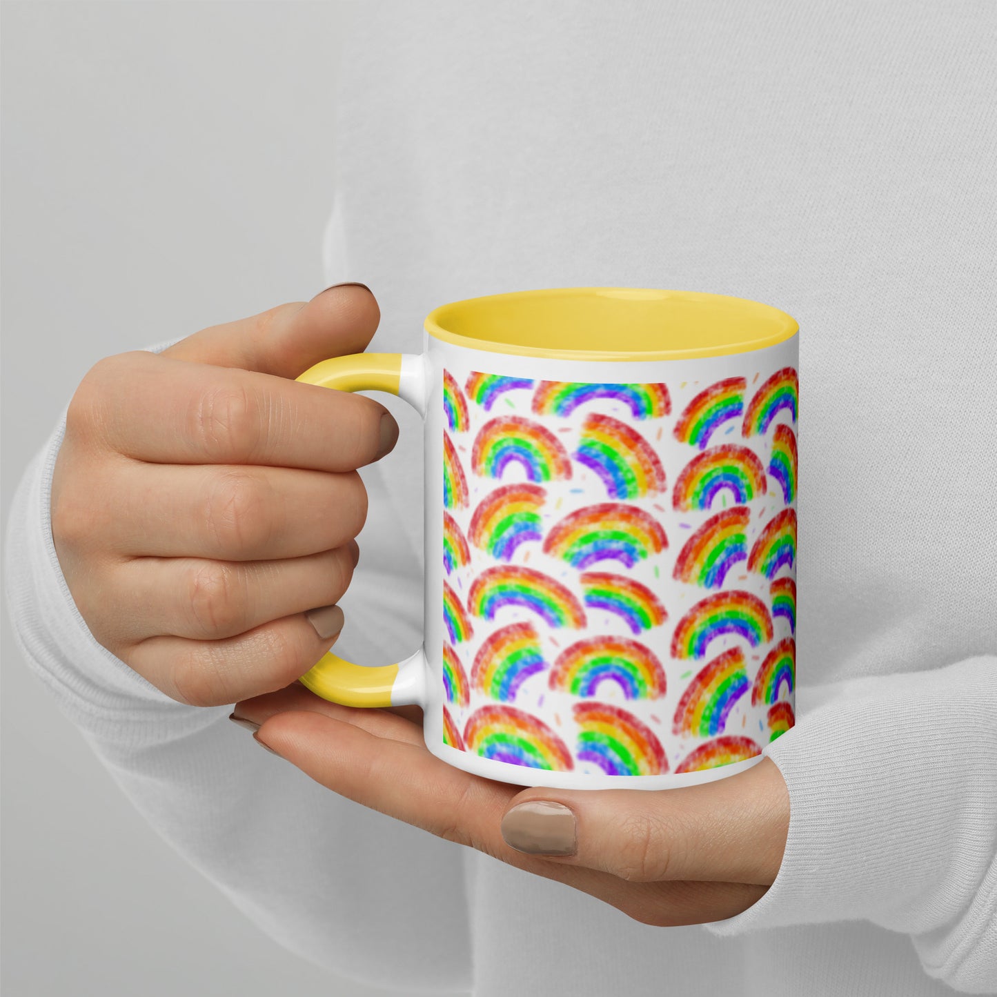 Mug with multi coloured rainbow pattern by Carmel Rimmer and a yellow interior held by a person against a plain background