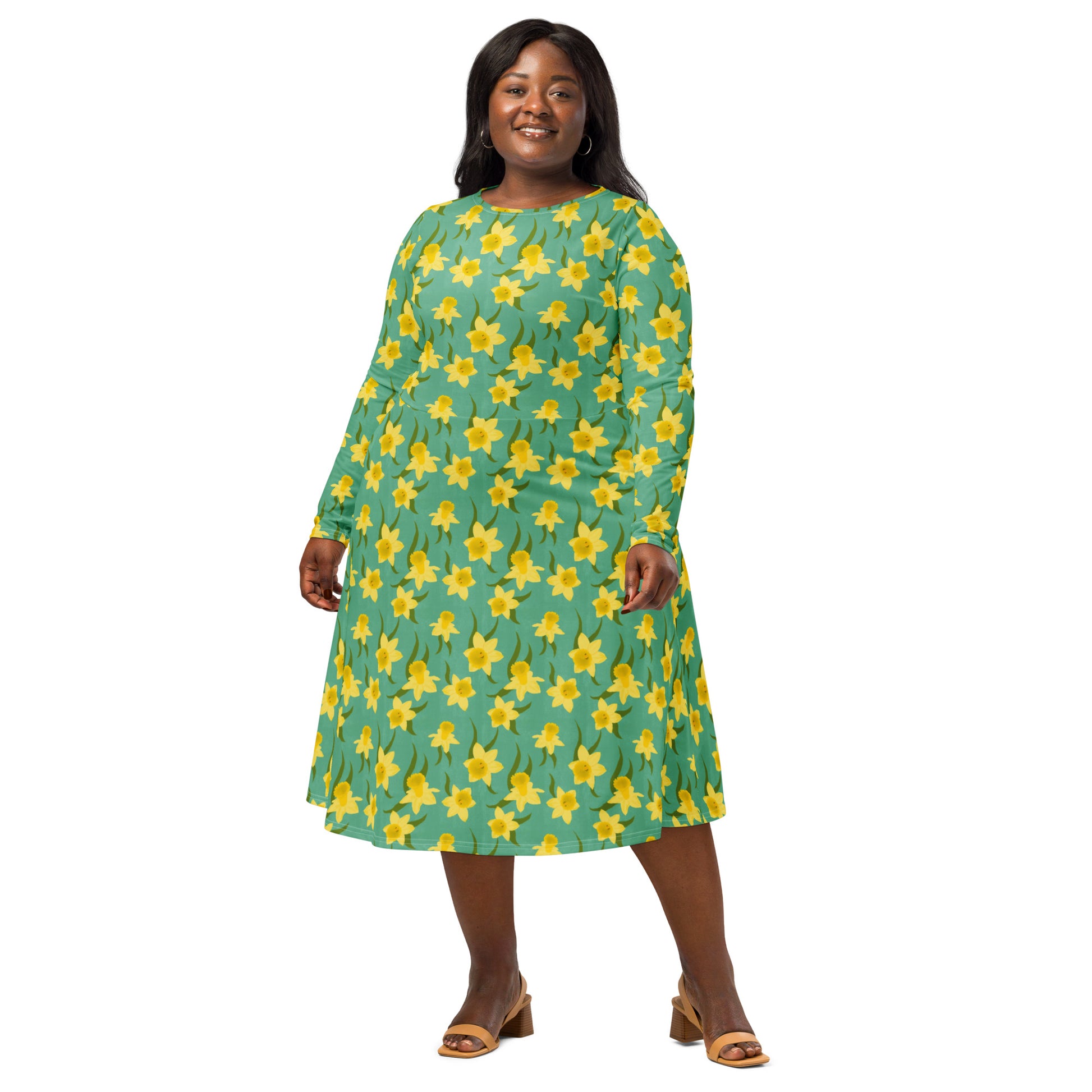 Woman wearing a green dress with yellow daffodil floral pattern by Carmel Rimmer, standing against a white background. 