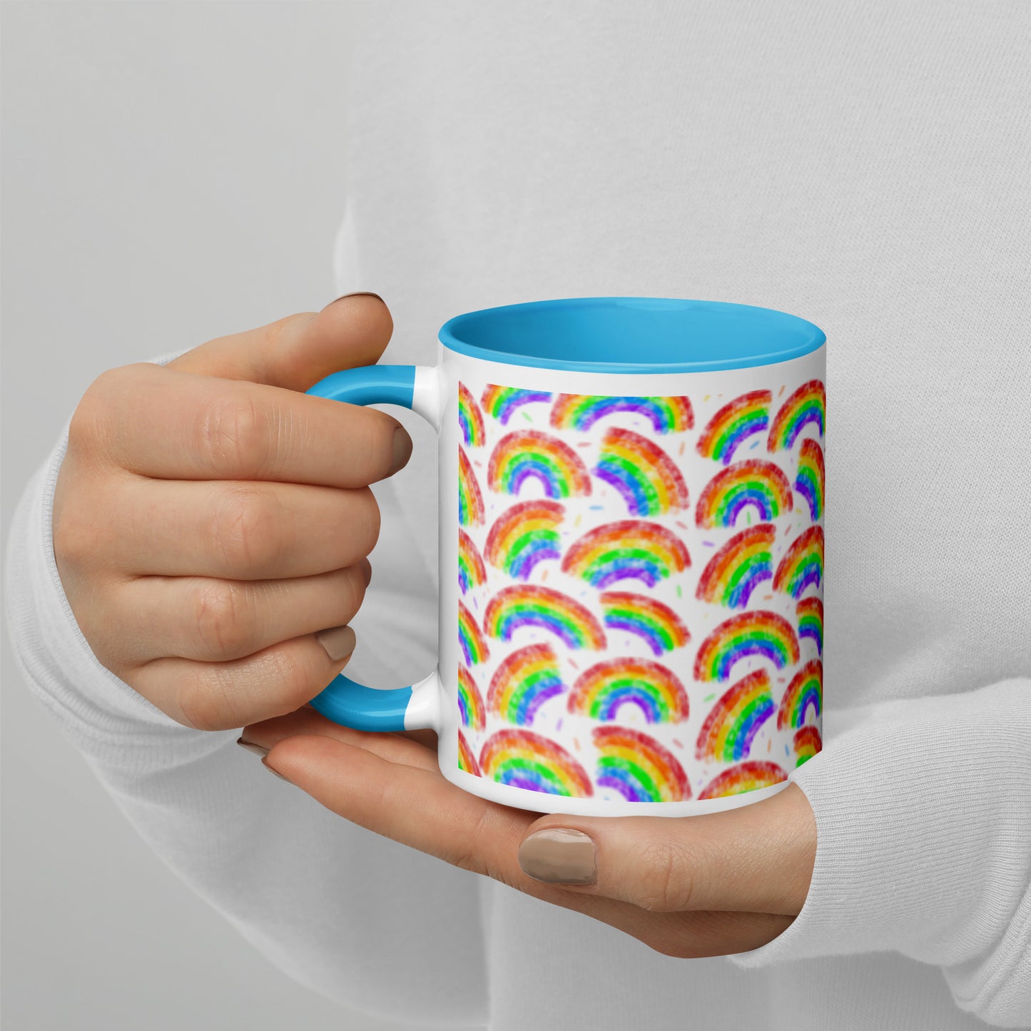 Mug with multi coloured rainbow pattern by Carmel Rimmer and a blue interior held by a person against a plain background