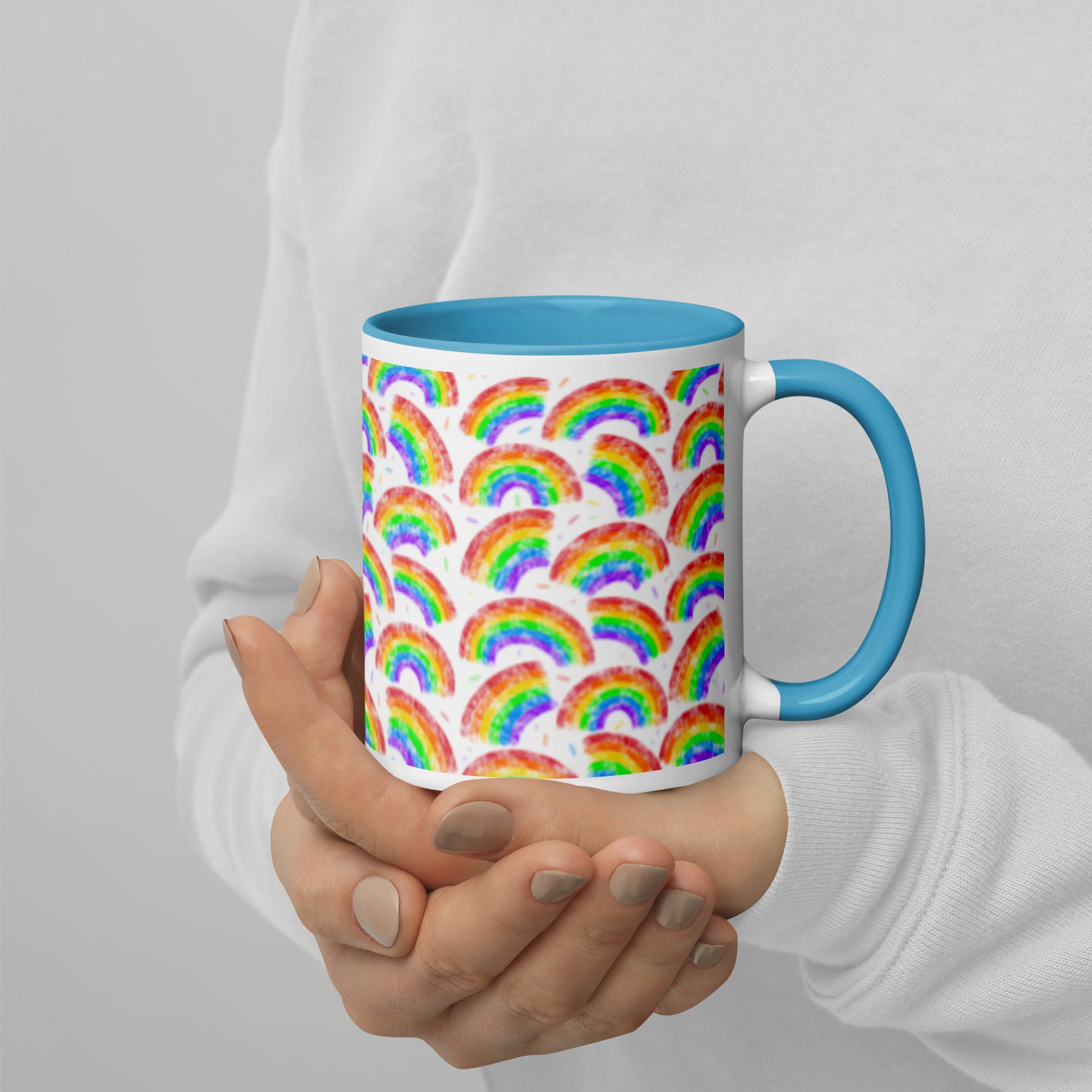 Mug with multi coloured rainbow pattern by Carmel Rimmer and a blue interior held by a person against a plain background