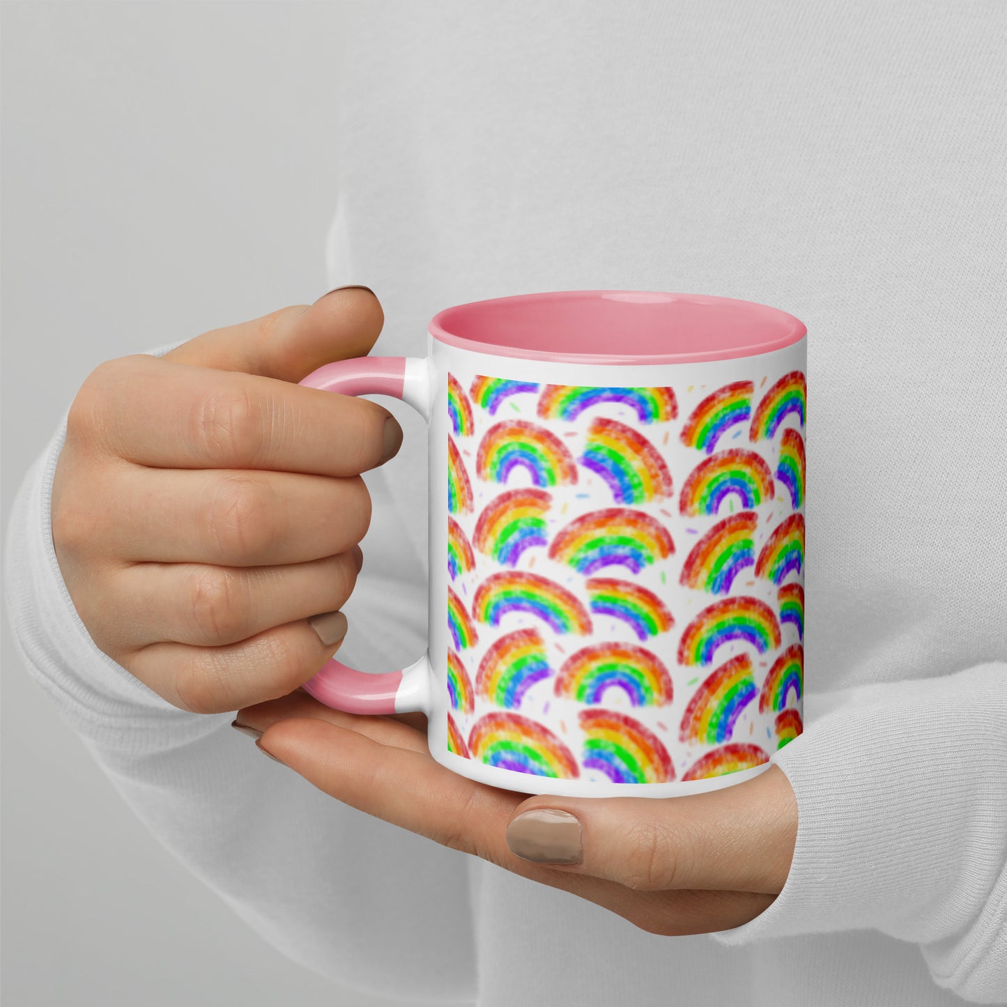 Mug with multi coloured rainbow pattern by Carmel Rimmer and a pink interior held by a person against a plain background