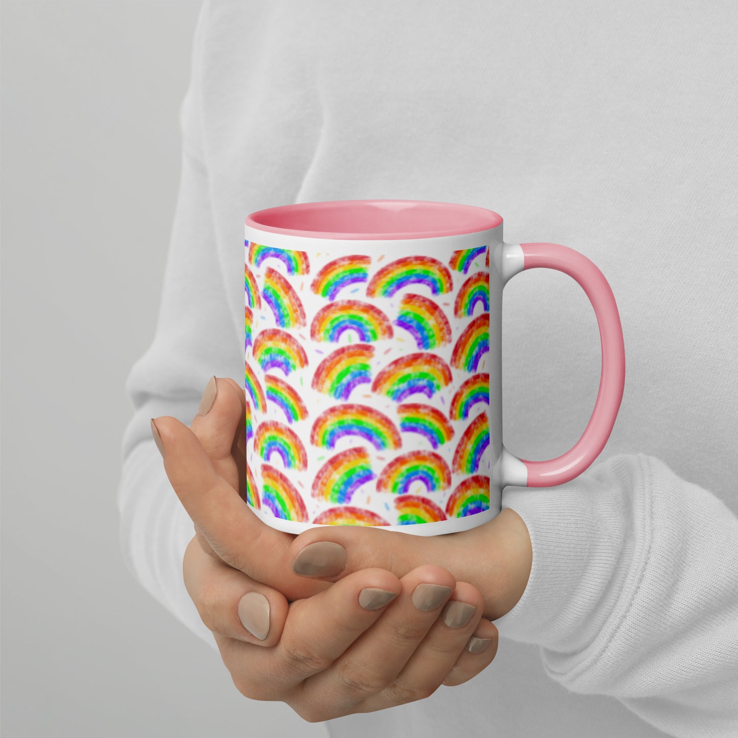 Mug with multi coloured rainbow pattern by Carmel Rimmer and a pink interior held by a person against a plain background