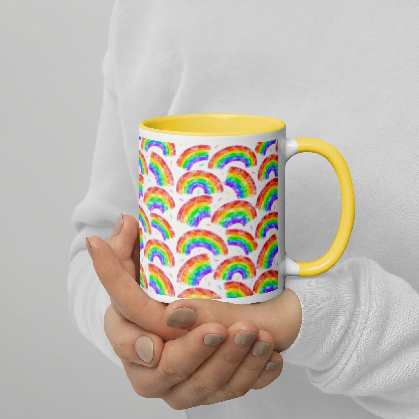 Mug with multi coloured rainbow pattern by Carmel Rimmer and a yellow interior held by a person against a plain background
