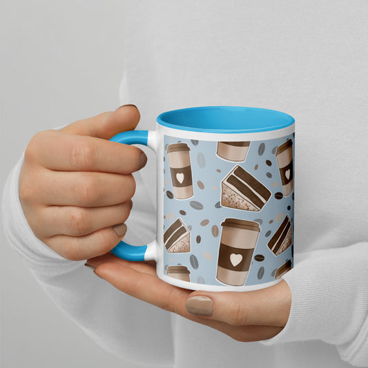 A ceramic mug with a 'Coffee & Cake' pattern by Carmel Rimmer and a blue rim and handle, being held in a person's hands.