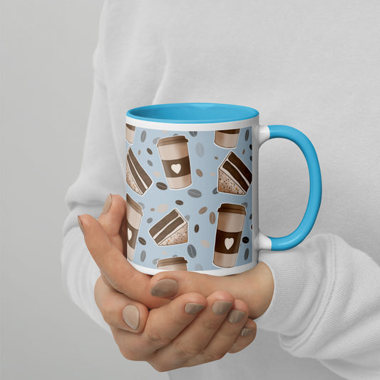 A ceramic mug with a 'Coffee & Cake' pattern by Carmel Rimmer and a blue rim and handle, being held in a person's hands.